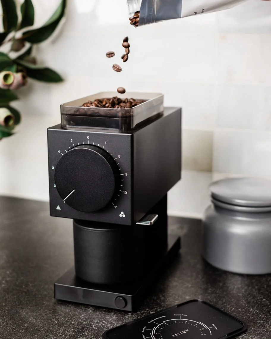 Coffee beans being poured into a coffee roaster machine on a kitchen countertop.