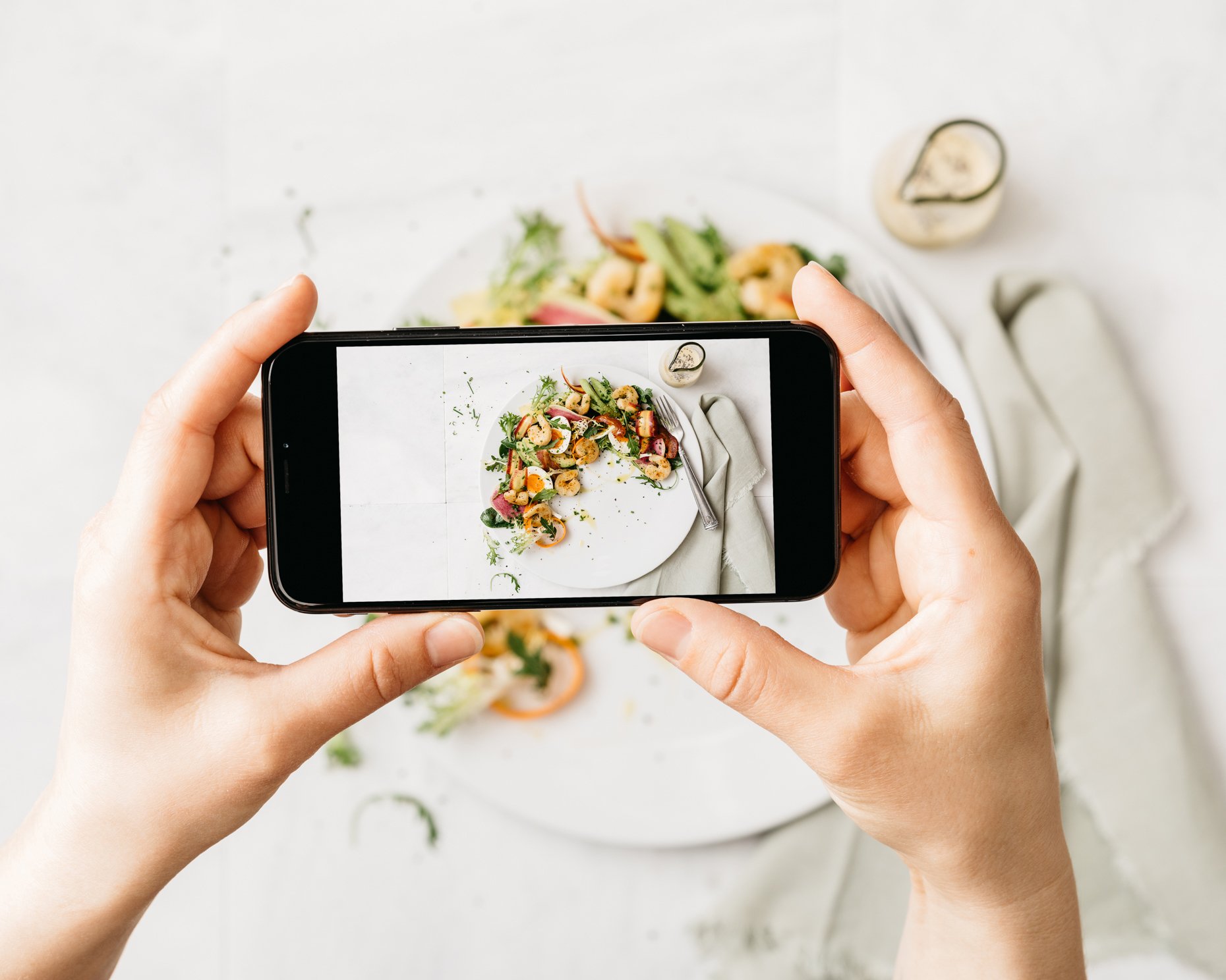 Person taking a photo of a plate of salad with a smartphone.