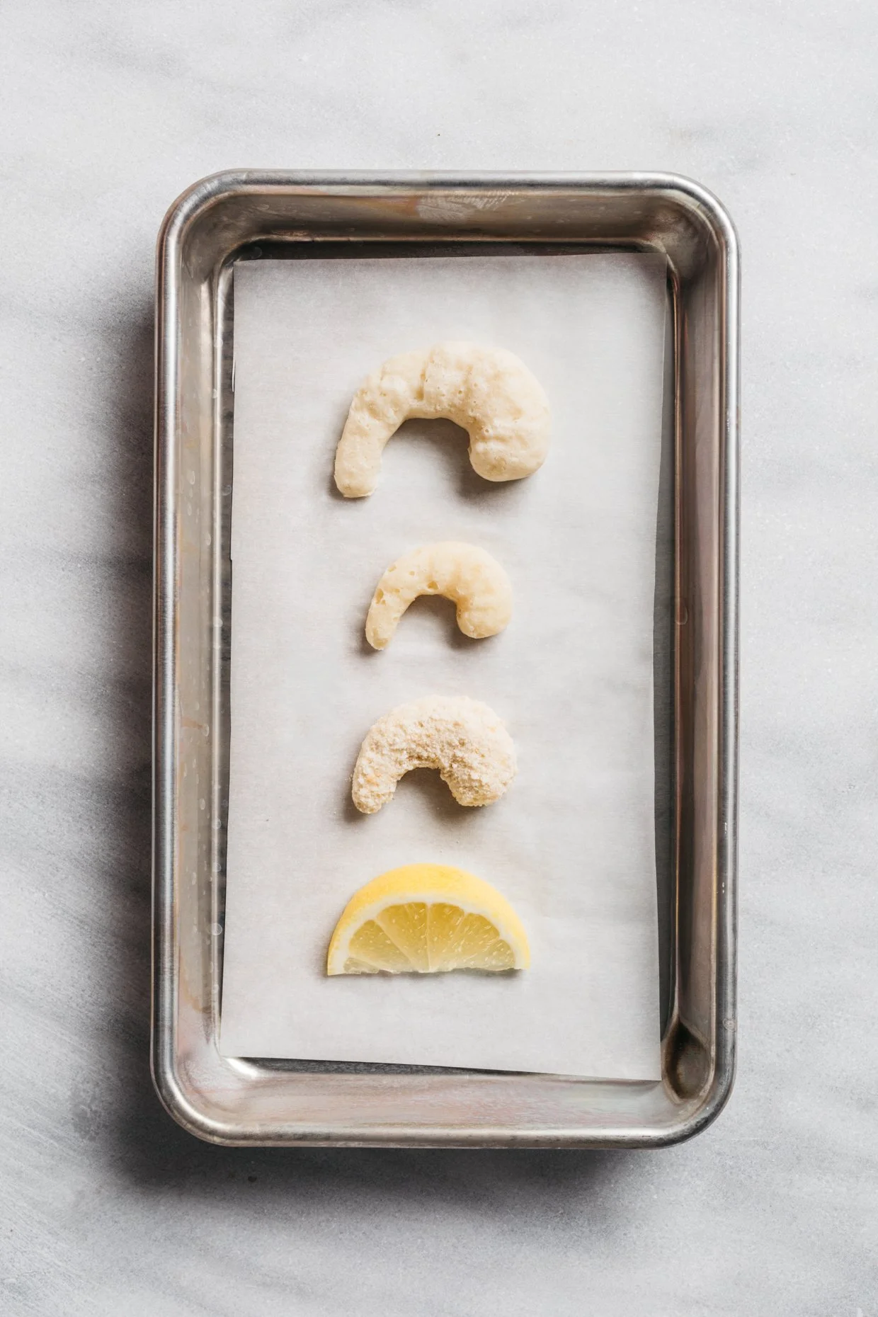 Four plant-based shrimp lined up on a silver baking tray with parchment paper, with a lemon wedge at the bottom.