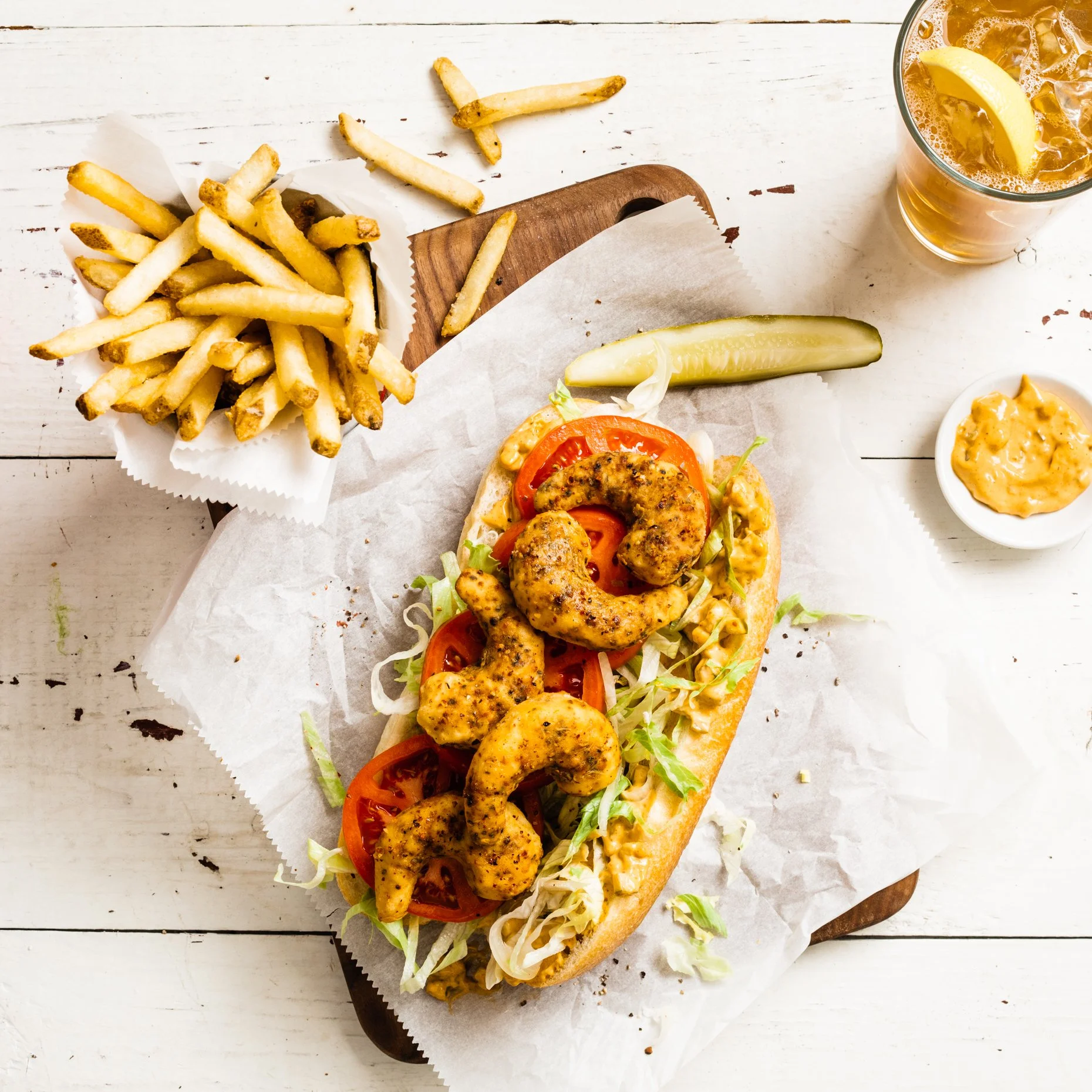 plant-based shrimp po' boy sandwich with French fries and iced tea on a white wooden table.