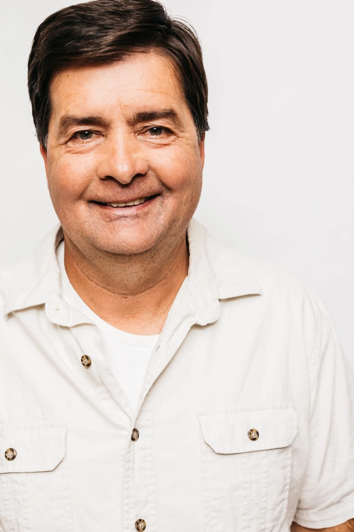 Portrait of a man smiling, wearing a white button-up shirt, against a plain white background.