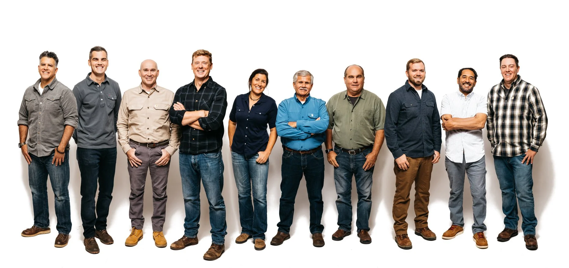 Group of twelve diverse adults standing against a white background, dressed casually and smiling.