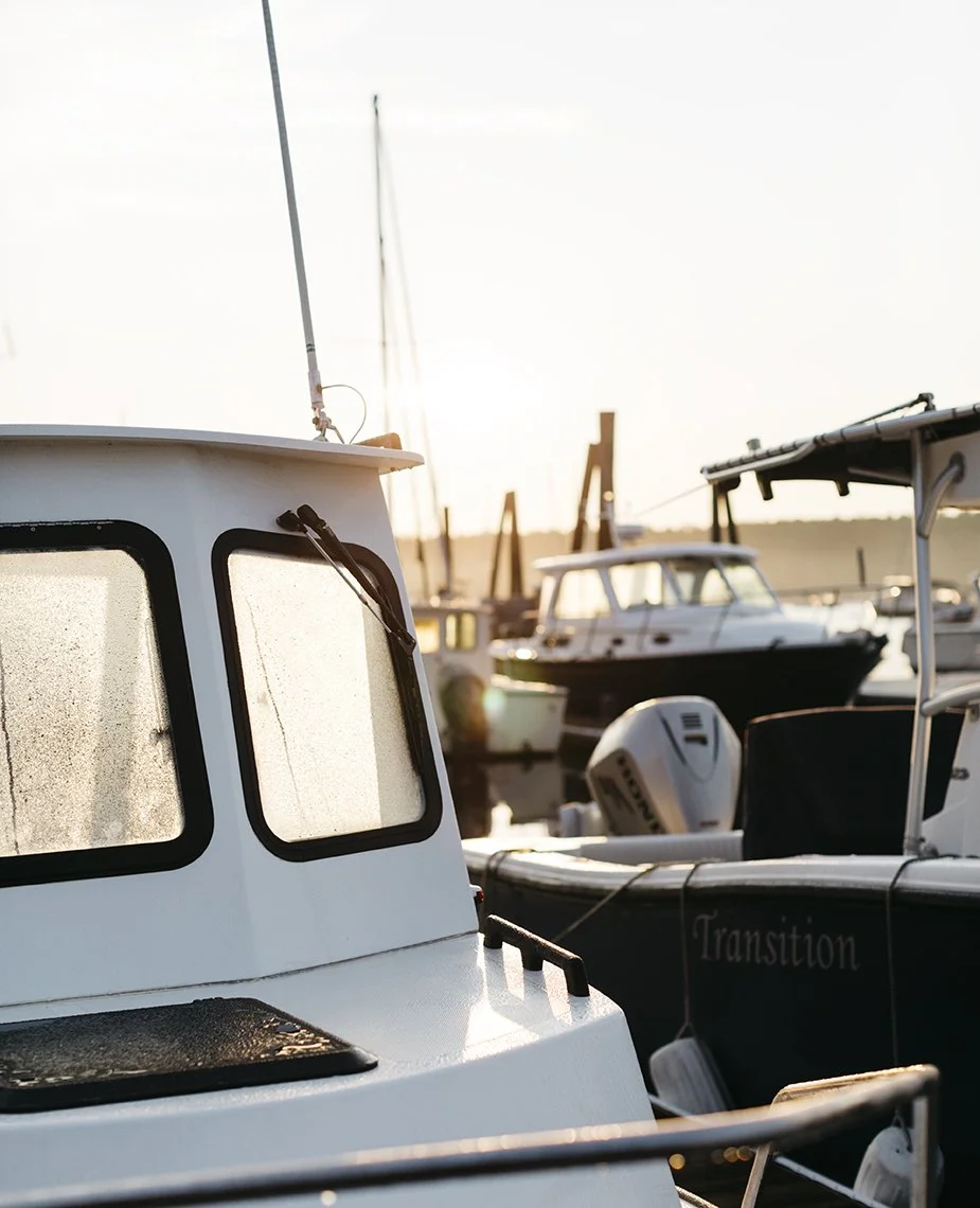 Close-up of a white boat with foggy windows docked at a marina during sunset, with other boats visible in the background.