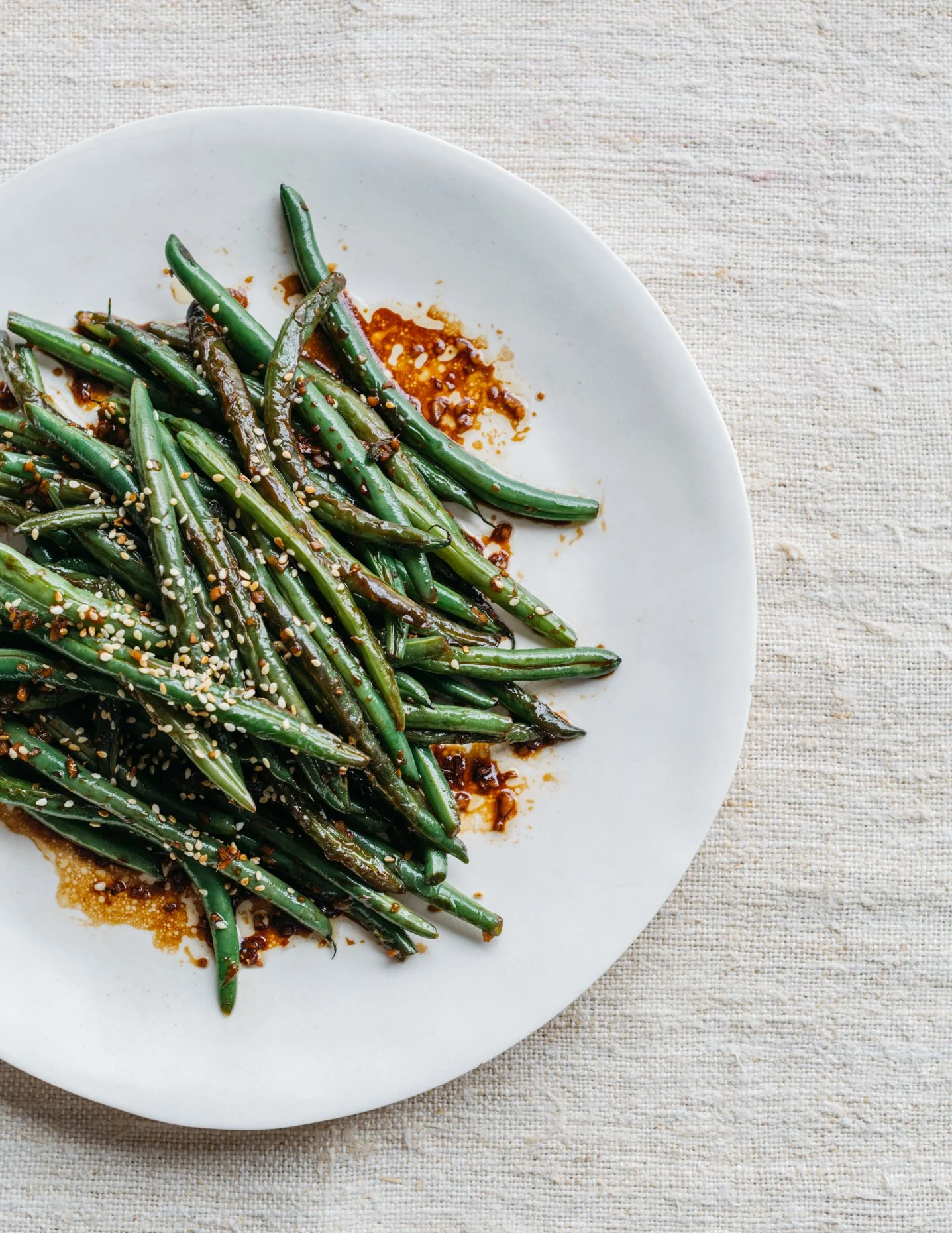 Green beans with sesame seeds and sauce on a white plate