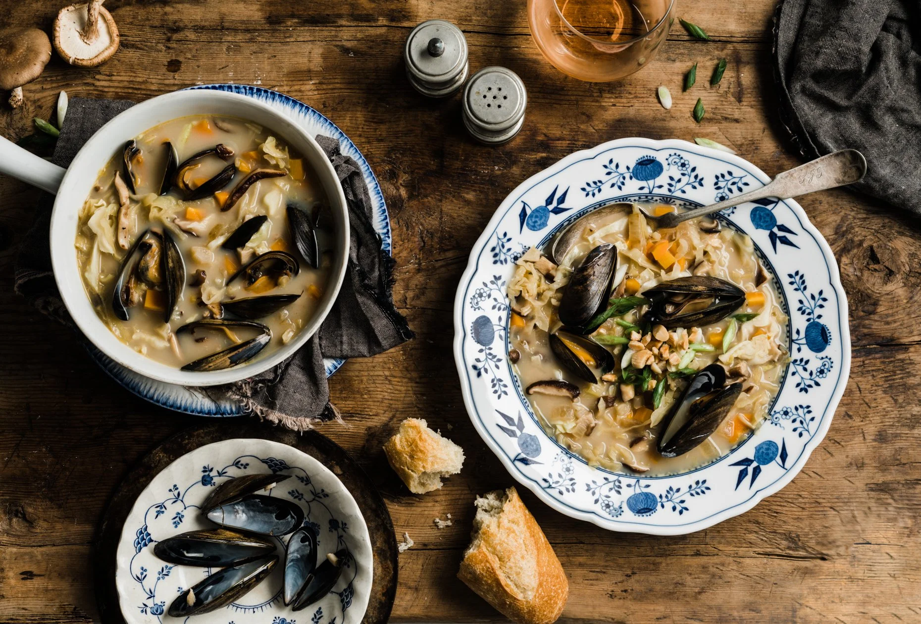 Bowl and plate of clam chowder soup with mussels, vegetables, and bread on a rustic wooden table.