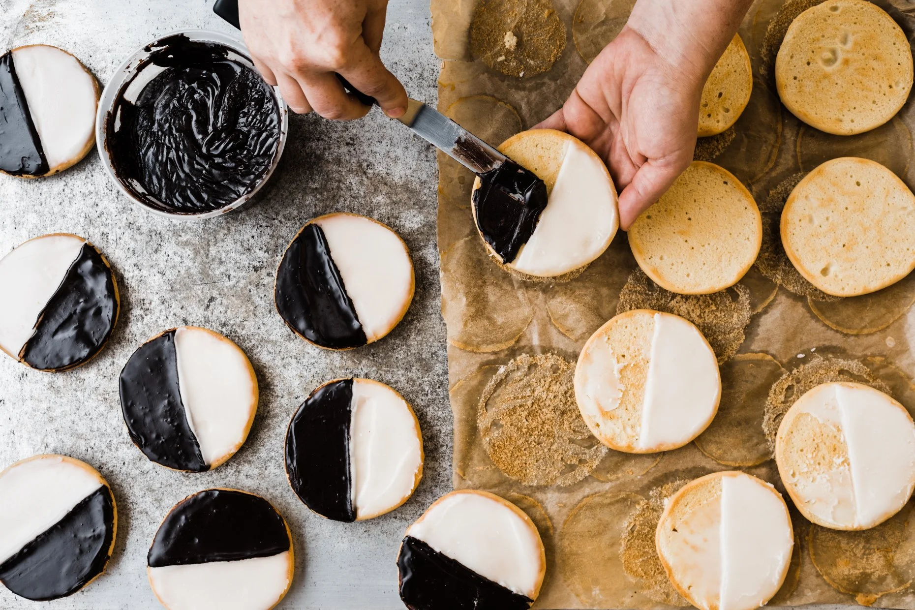 Person decorating cookies with black and white icing, cookies arranged on parchment paper and a tray.