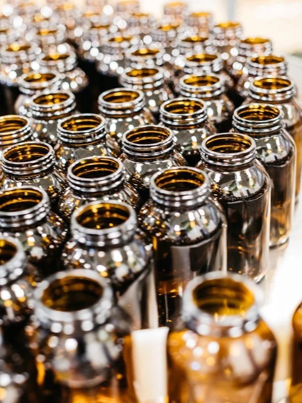Multiple rows of small amber glass bottles without caps, arranged on a surface.