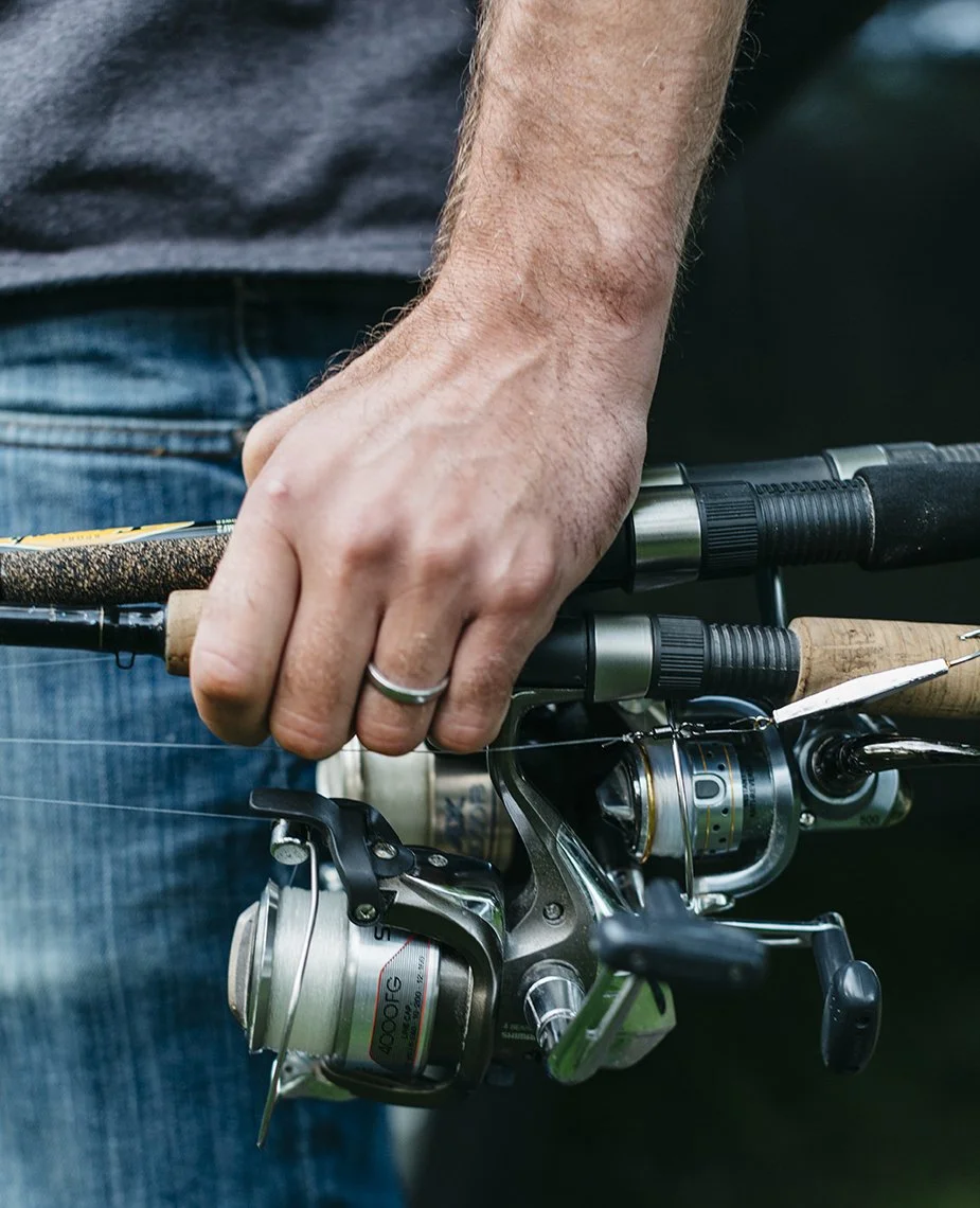 Close-up of a person holding a fishing rod with a reel, wearing a ring on their finger.