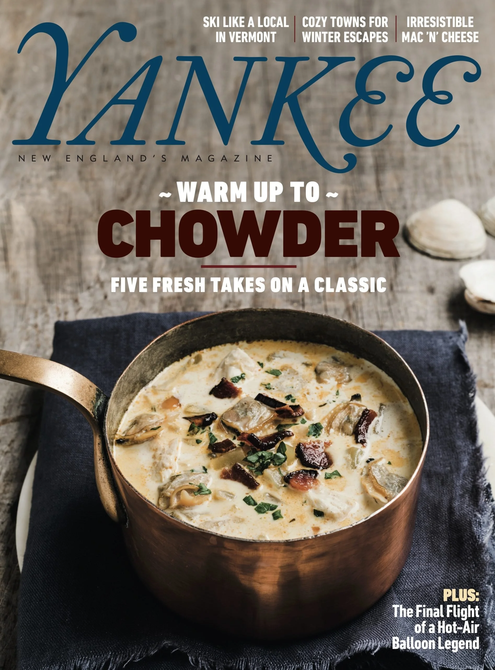 Cover of Yankee magazine featuring a pot of clam chowder on a wooden surface with seashells nearby and a dark cloth underneath. The magazine promotes winter escapes and local Vermont skiing.