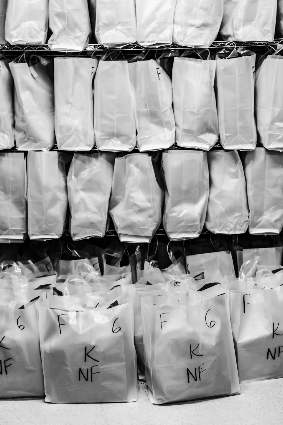 Stacked white paper gift bags on wire shelving, some with black handwritten markings.