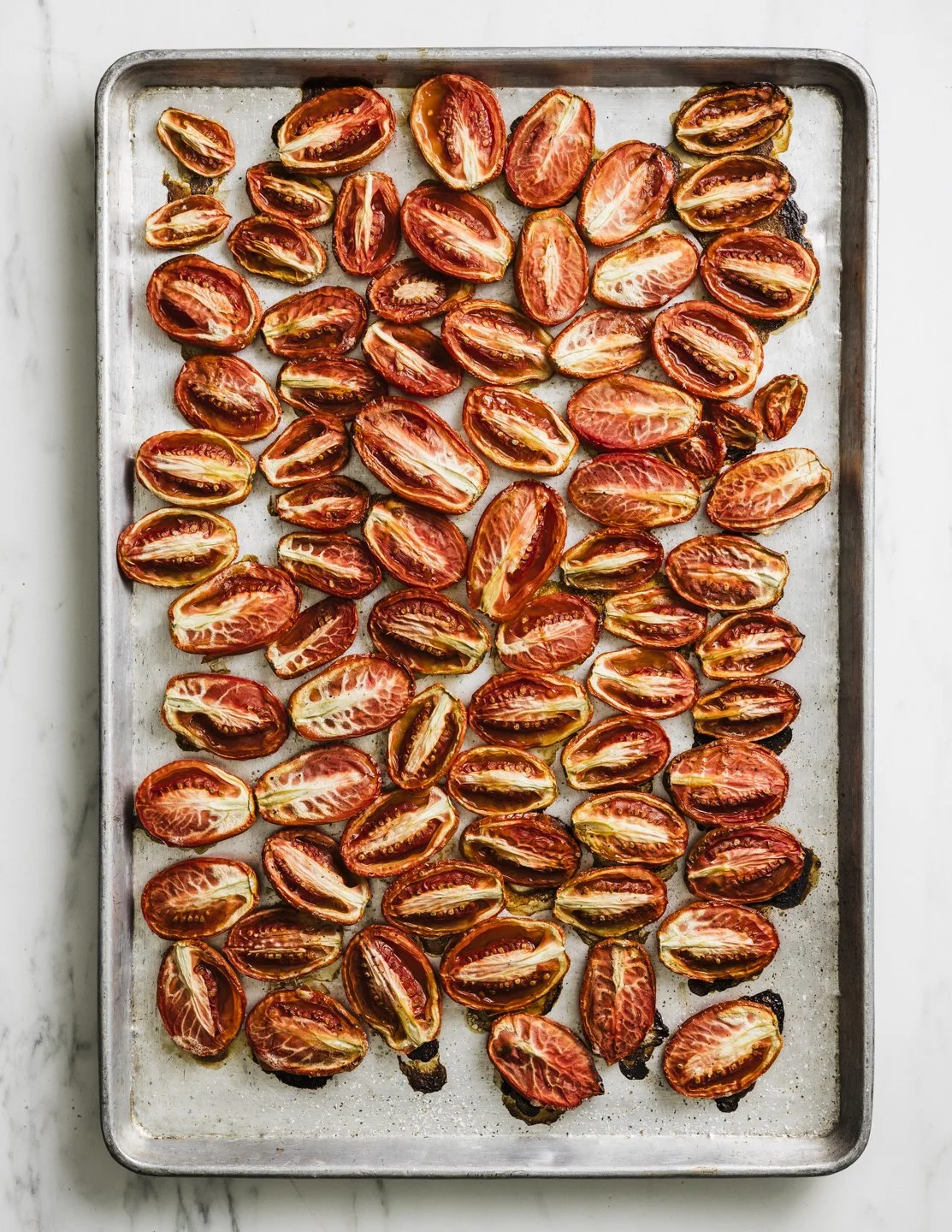 A baking sheet filled with halved cherry tomatoes, some roasted with charred edges.