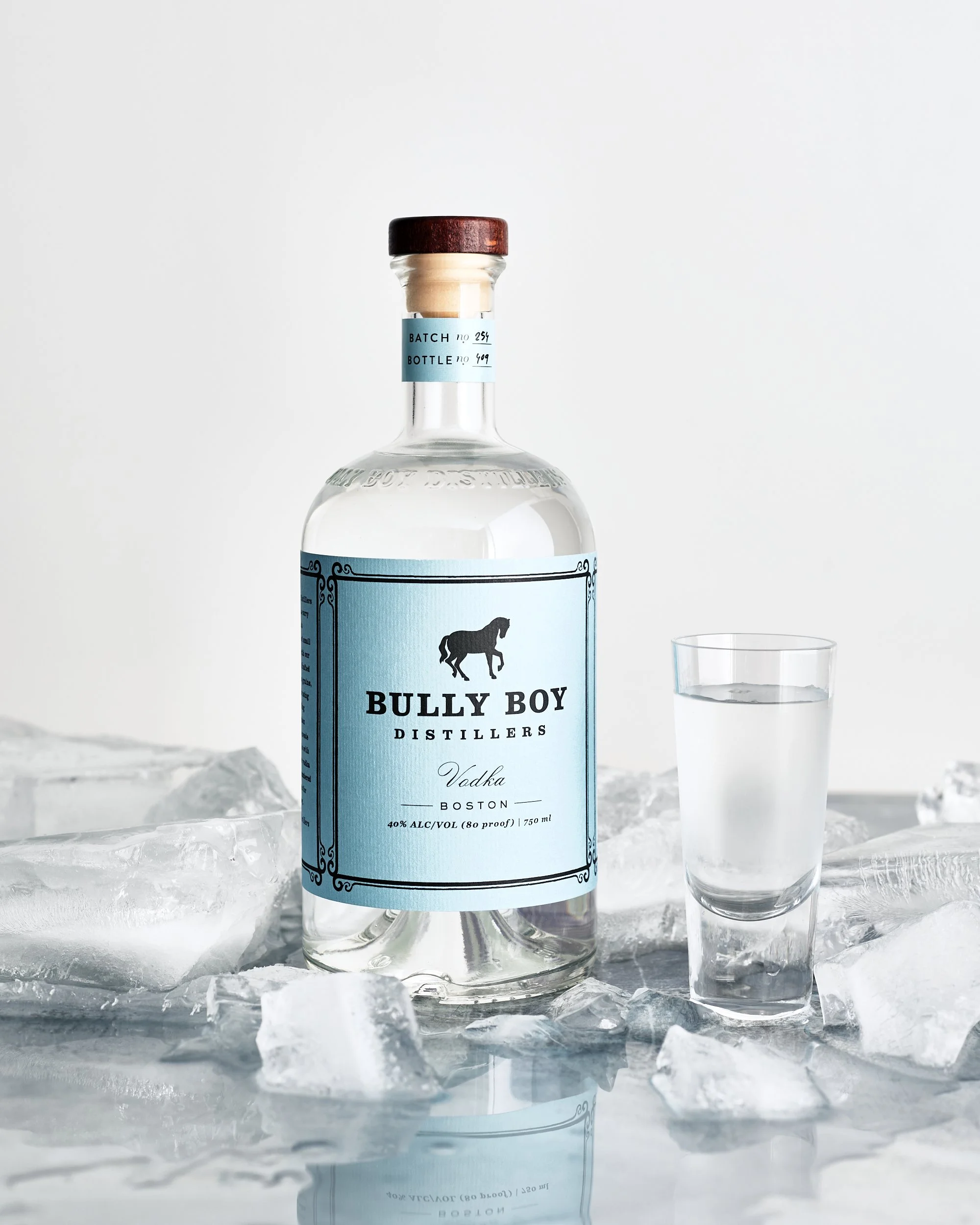 A bottle of Bully Boy Vodka with a glass of clear liquid placed on ice.