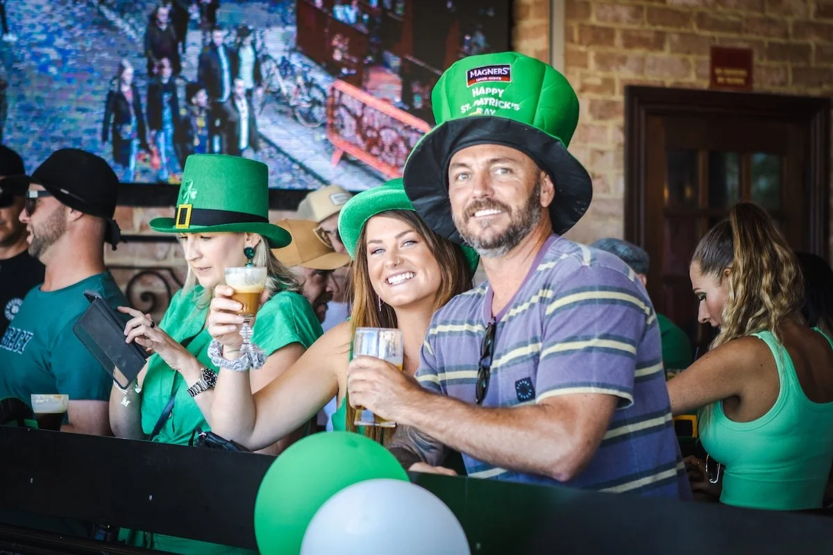 People celebrating St. Patrick's Day at a bar, wearing green hats and clothing, and holding drinks.