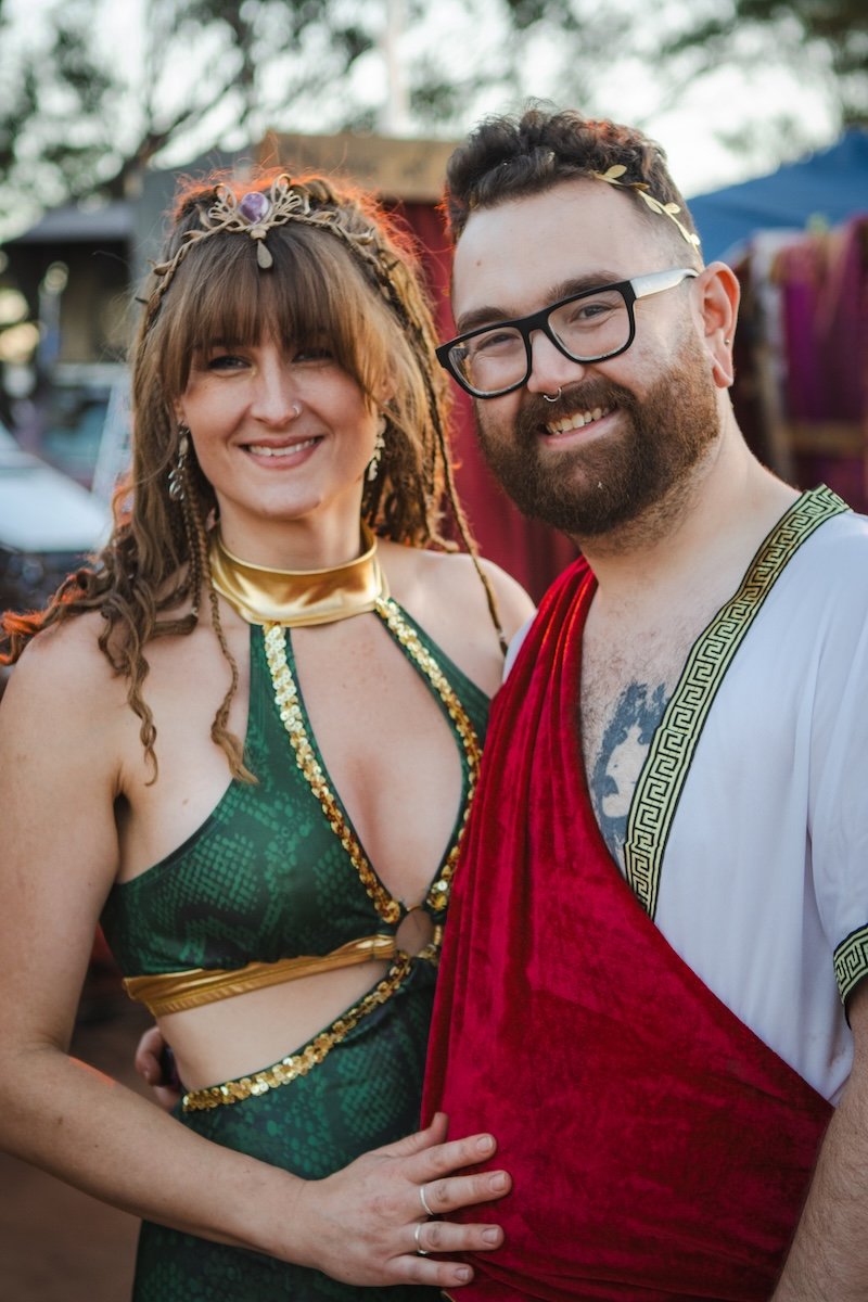 Two people dressed in costumes standing outdoors, smiling at the camera.