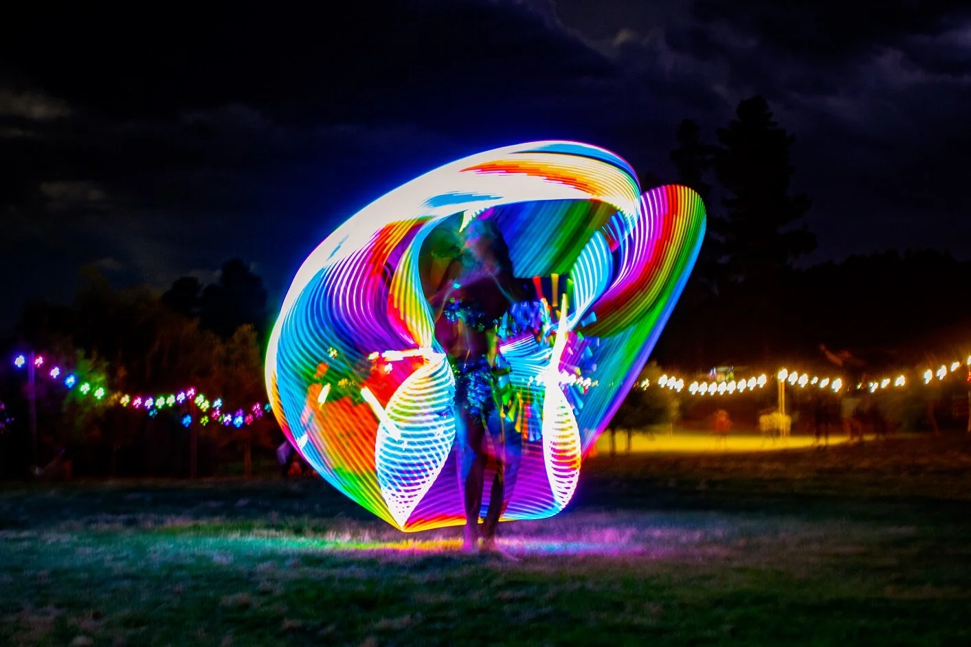Person performing with LED hula hoops creating colorful light trails at night.