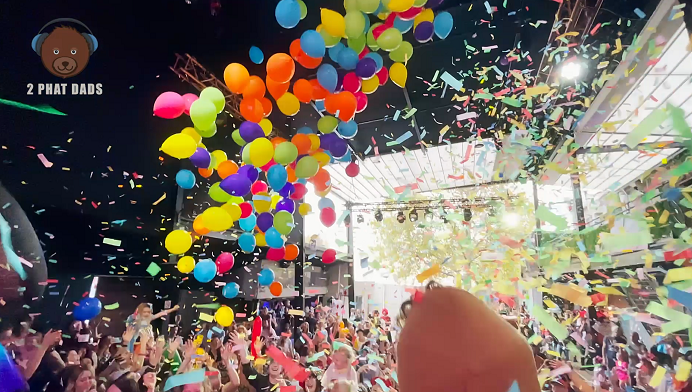 Colorful balloons and confetti falling at a lively celebration or party with a crowd of people in an indoor venue.