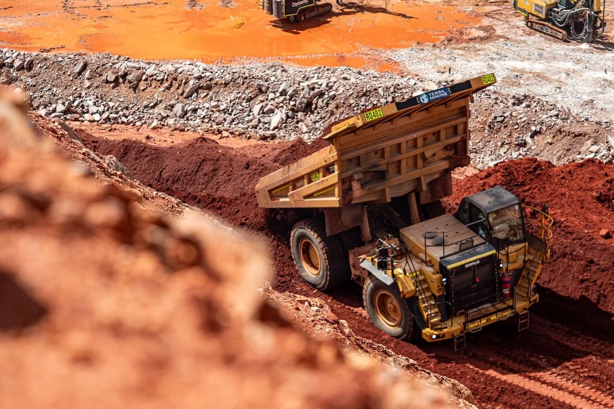 A large yellow dump truck unloading dirt on a construction site with machinery and dirt mounds in the background.