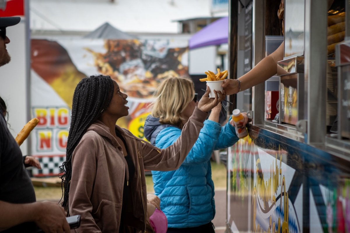 People ordering food at a fast food truck, with one woman receiving a cup of French fries from the server.