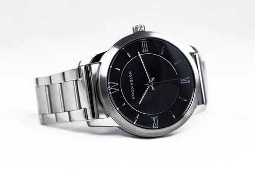 Silver wristwatch with black dial and Roman numerals, displaying time, with the brand name "VOGUEBRAND" on the face.