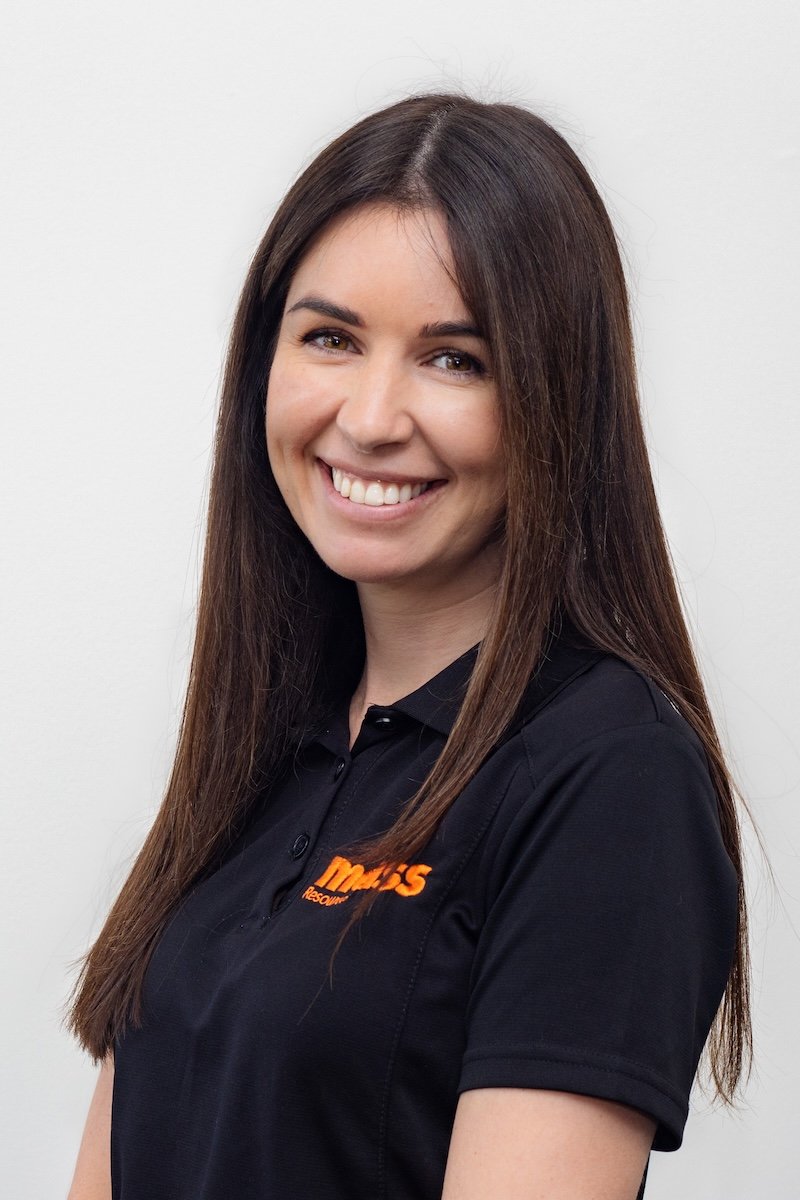 A woman with long brown hair smiling in front of a white background, wearing a black polo shirt with orange text and logo.