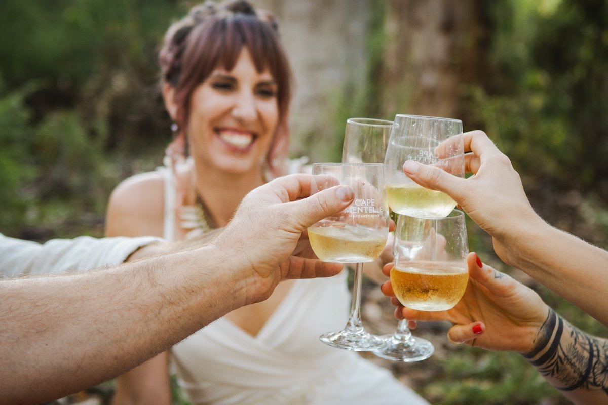 Group of people holding wine glasses with white wine in an outdoor setting, smiling and toasting.