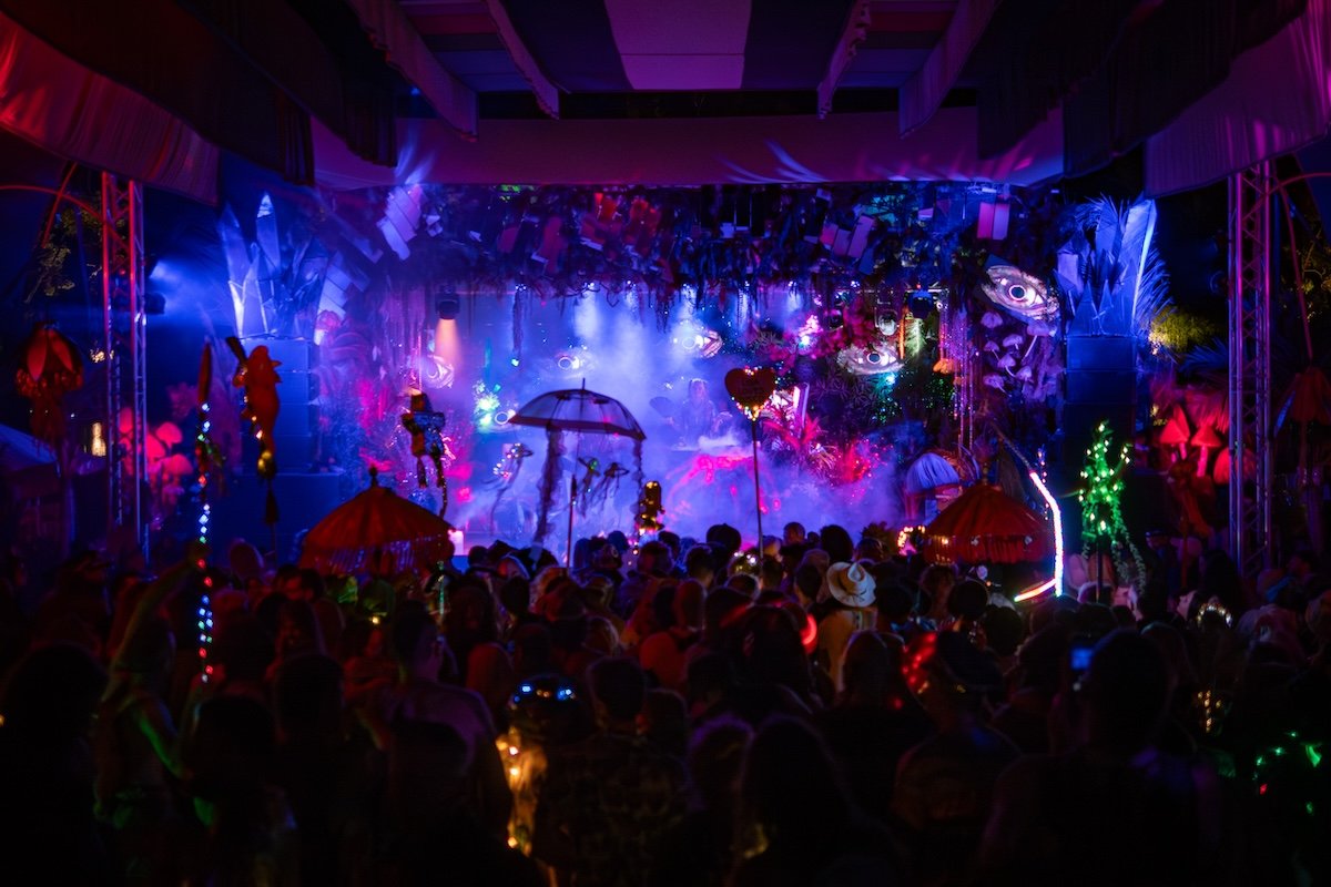A vibrant stage with colorful lights and decorations, crowded with people attending a concert or event at night.