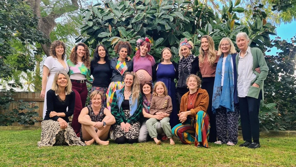 Group of people standing and sitting outdoors in front of greenery, smiling for a photo.