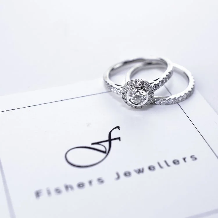 Two diamond rings, one with a large center stone, resting on a paper with the 'Fishers Jewelers' logo.