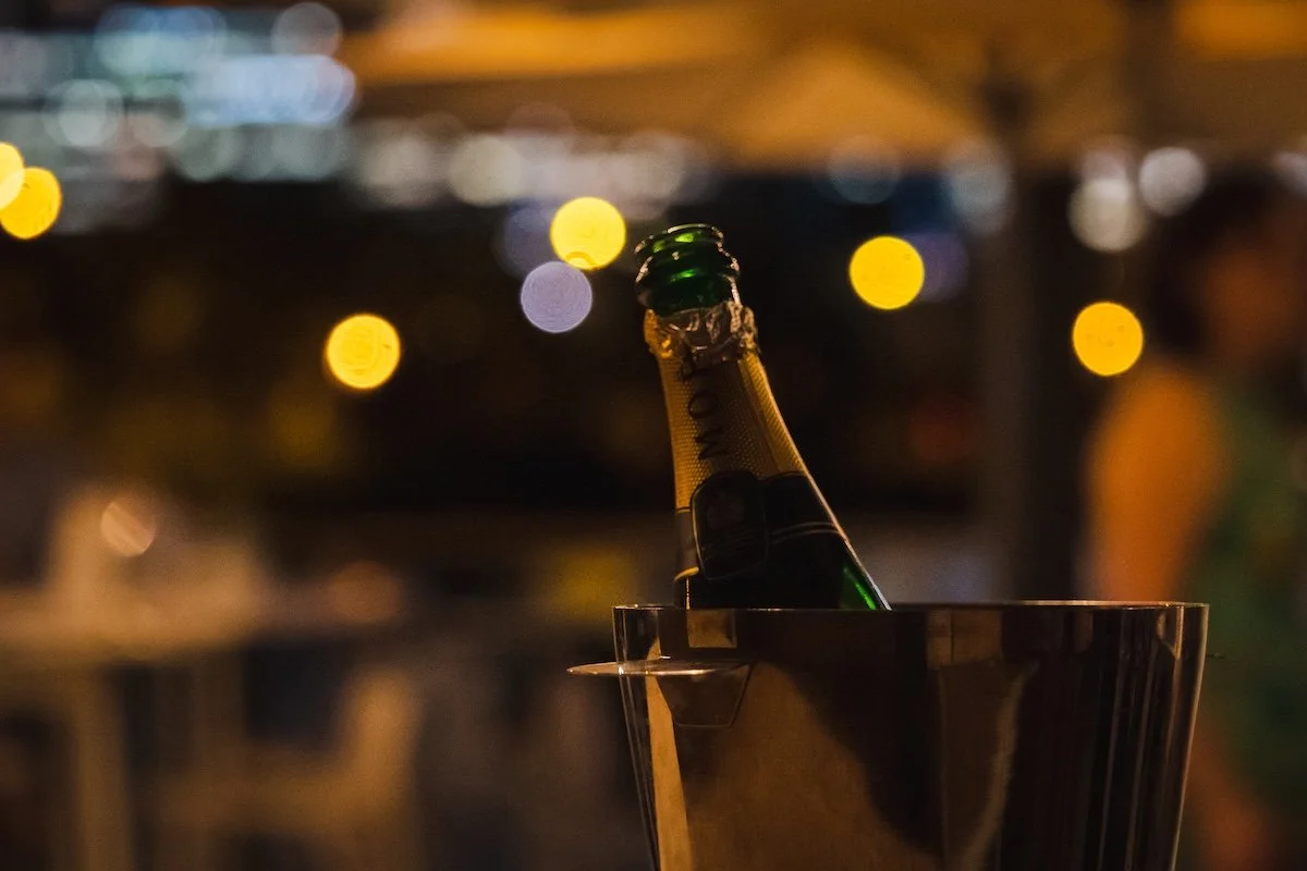 A bottle of champagne chilling in an ice bucket at a nighttime event with blurred lights and people in the background.