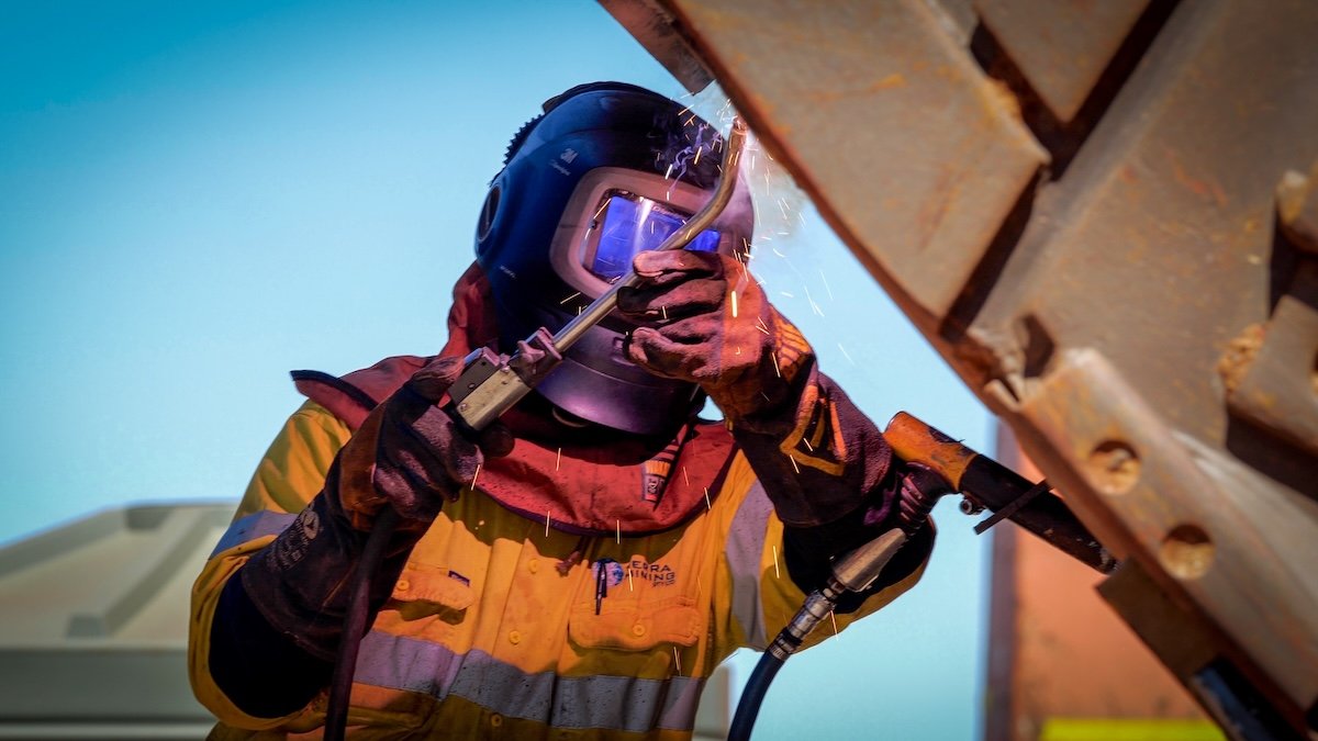 A welder wearing a protective helmet and gloves, welding metal components with sparks flying.