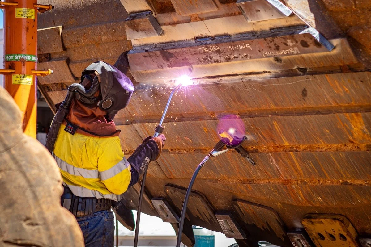 A worker wearing protective gear welding a large metal structure with sparks flying in an industrial workshop.