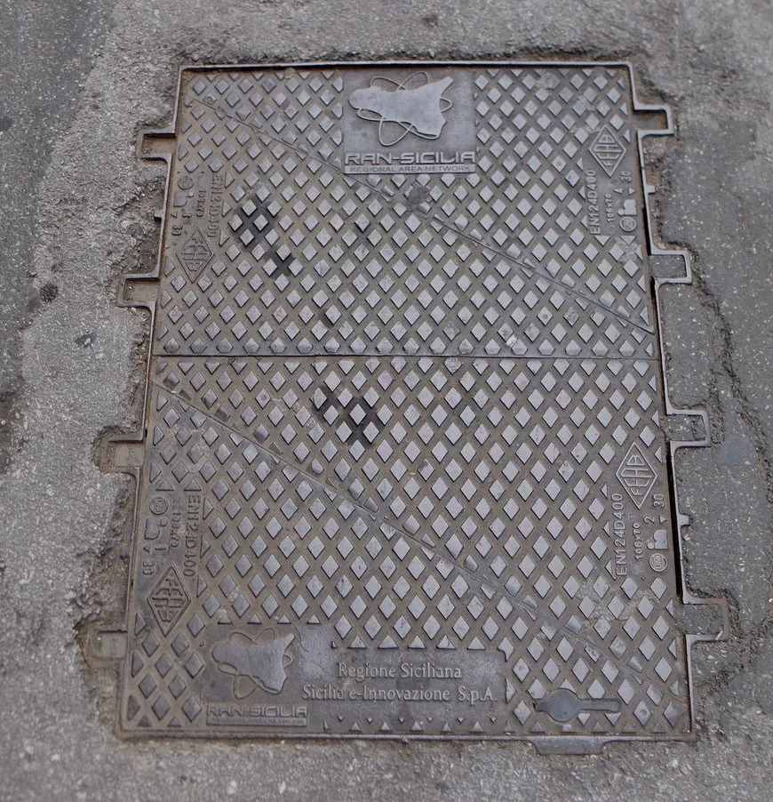 “The largest covers sit over big valves and vaults containing transformers. Rectangular split covers are most often used for this purpose.” MANHOLE COVERS by Mimi & Robert Melnick - 1994 Palermo, Sicily, Italy.