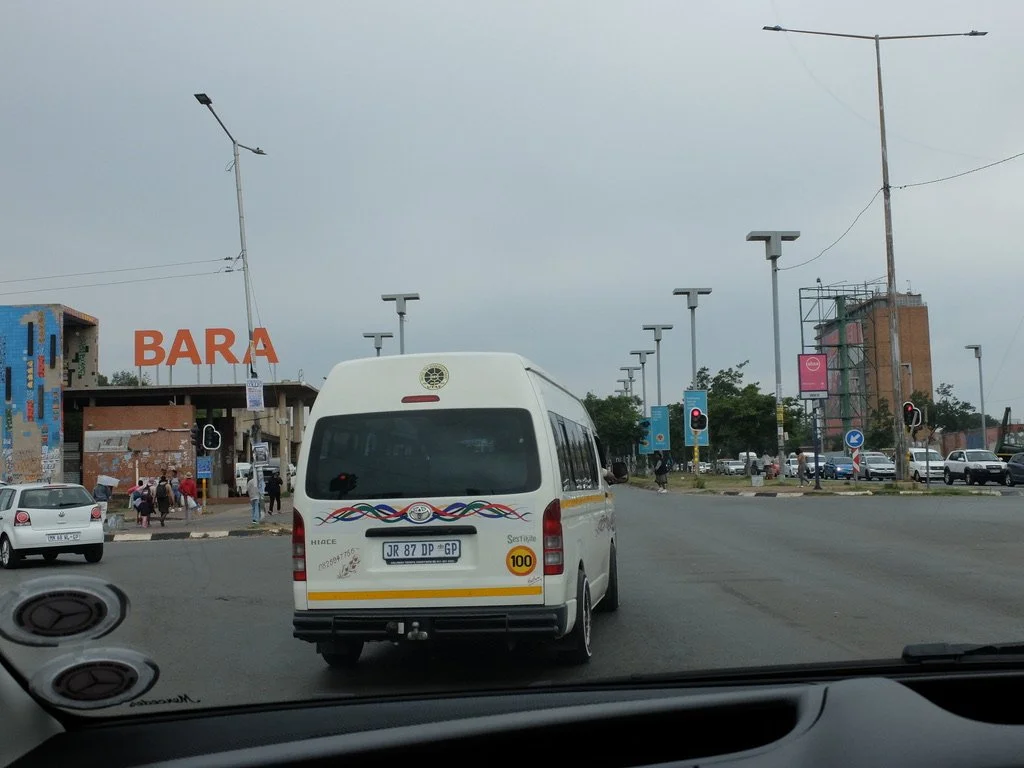  There is no mass transit system in South Africa; it’s too dangerous for the passengers.  Instead, these vans which hold fifteen passengers, taxi folks around.  Each driver  has a route &amp; has to stick to it.  The round decal on top is their union