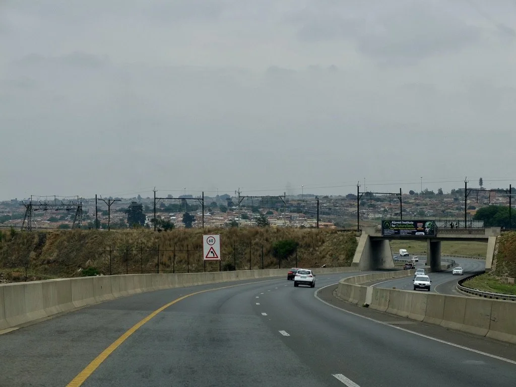  That’s Soweto ahead.  “The establishment of Apartheid in 1948 cemented racial divisions.  New townships, such as the infamous  Soweto (So uth Western Township), were built on exposed land to the south of t he min es and subject to the winds. Whites 