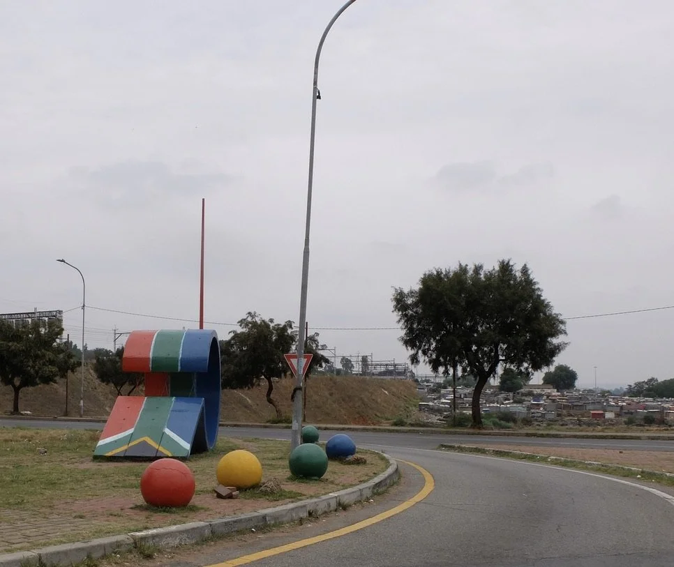  It’s like everywhere you turn, there are acres &amp; acres of these shacks. I was intrigued by the roundabout art then noticed the shacks to the right.  Joburg, ZA. 