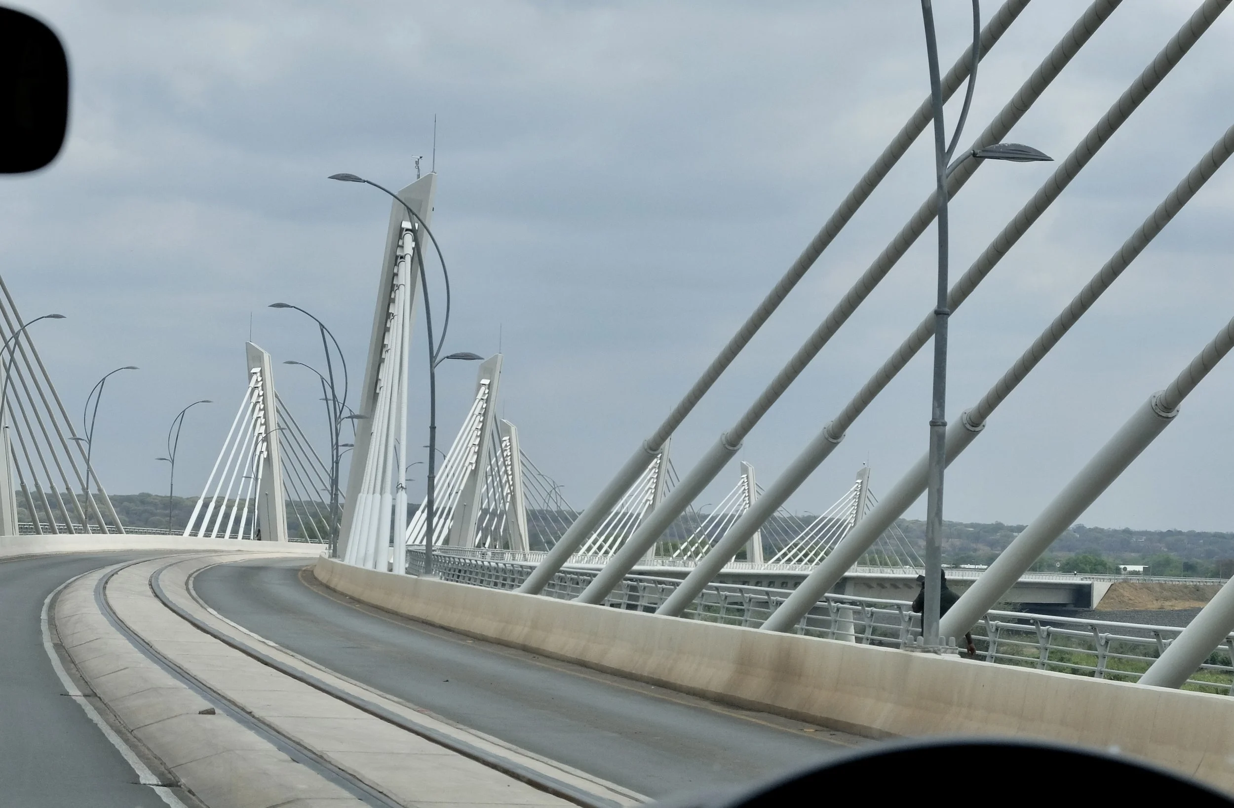  The ca. 2021 Kazungula Bridge with two motor vehicle traffic lanes, a railroad line &amp; pedestrian lanes. “Before the bridge existed, traffic flowed slowly across the river on unreliable ferries. Trucks waited as long as 12 days to get on a pontoo