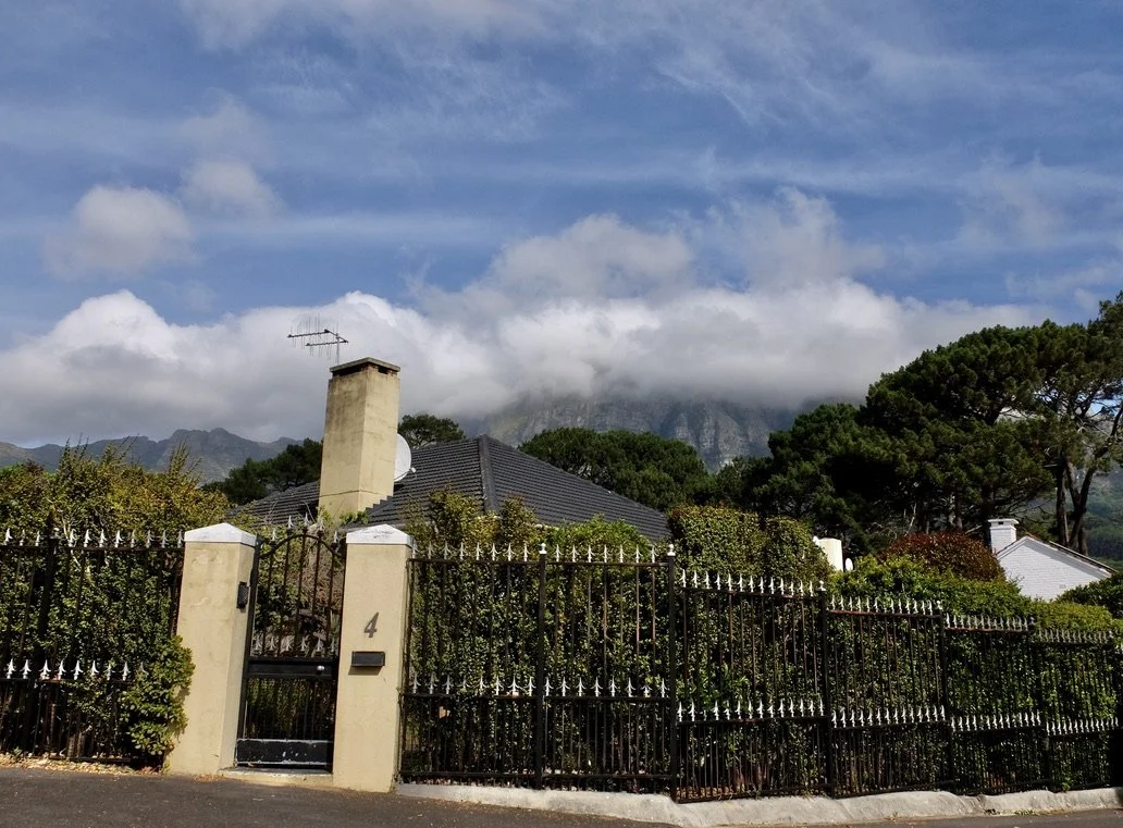  In  the Bishopscourt upscale neighborhood seen in Cape Fusion Tours, Cape Town Eats Tour with Karin Schmidt.  Nelson Mandela lived in this ‘hood when he was president.  Note the electrified wire atop the fencing.    That’s Table Mountain enveloped i