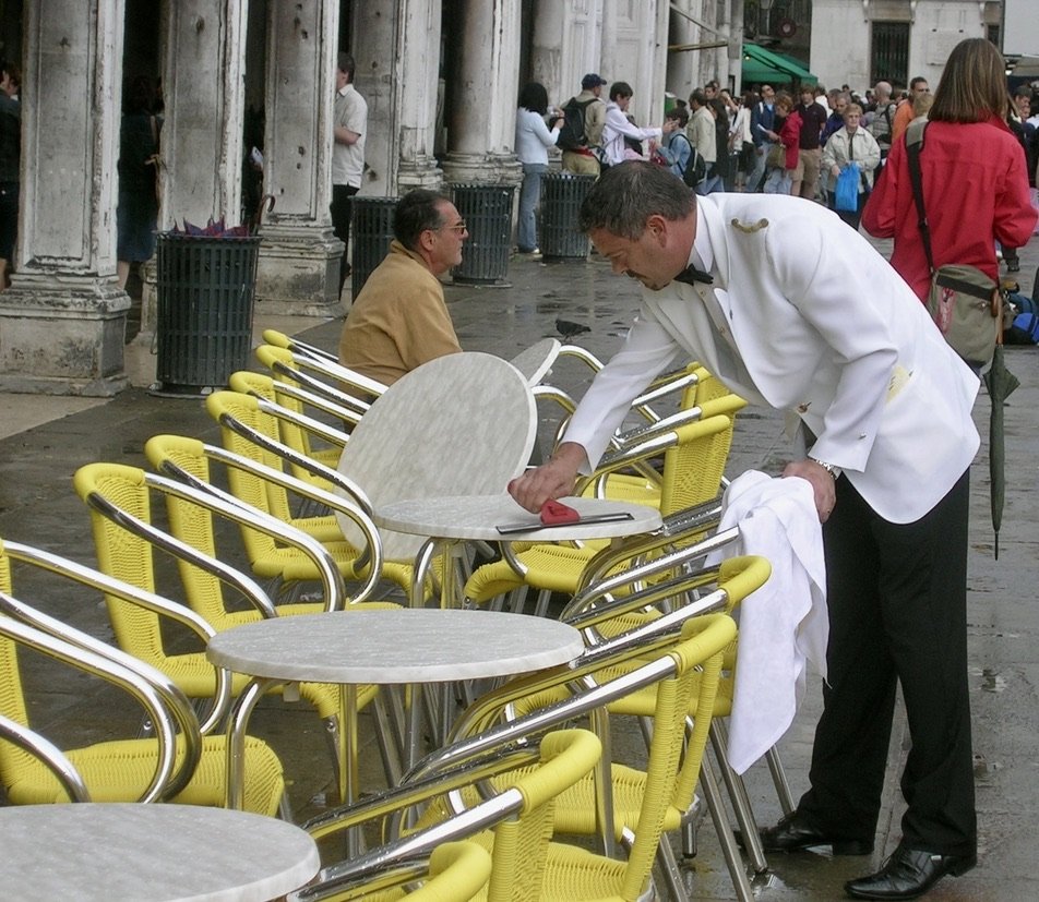  I was drawn in by the yellow &amp; line of the tables in Piazza San Marco, Venice, Italy.&nbsp; I love to capture workers.&nbsp; He’s so dapper from the fresh pressed uniform down to the polished dress shoes. Nikon Cool Pix P7100.  People in the pho