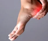 A hand holding a red heating pad against a person's ankle.