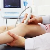 Healthcare professional using ultrasound device on patient's leg.