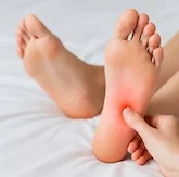 Close-up of a person's foot with a person massaging or pressing the sole, showing some redness on the heel.