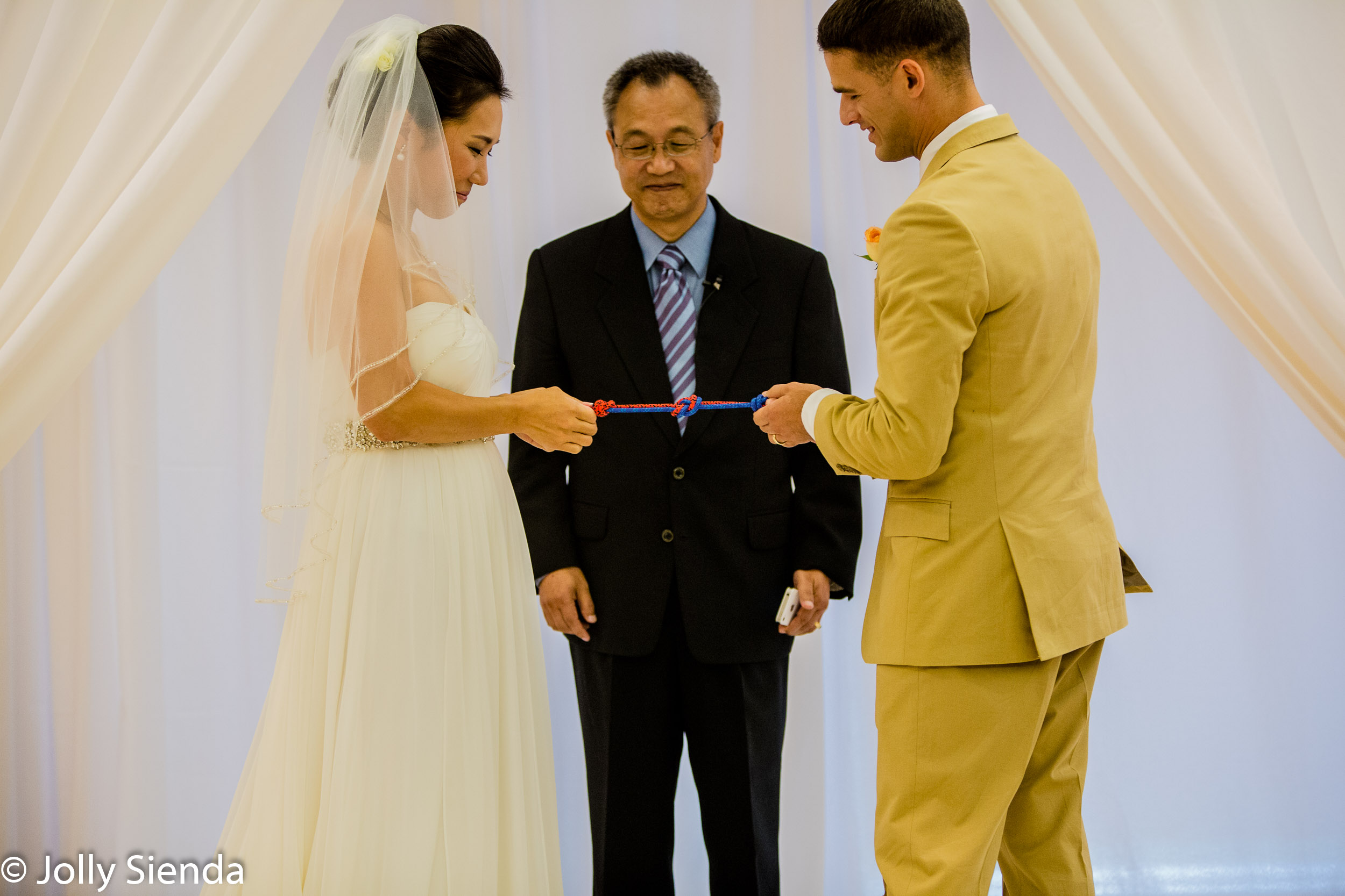 Portrait of a bride and groom tieing the knot at the wedding alt