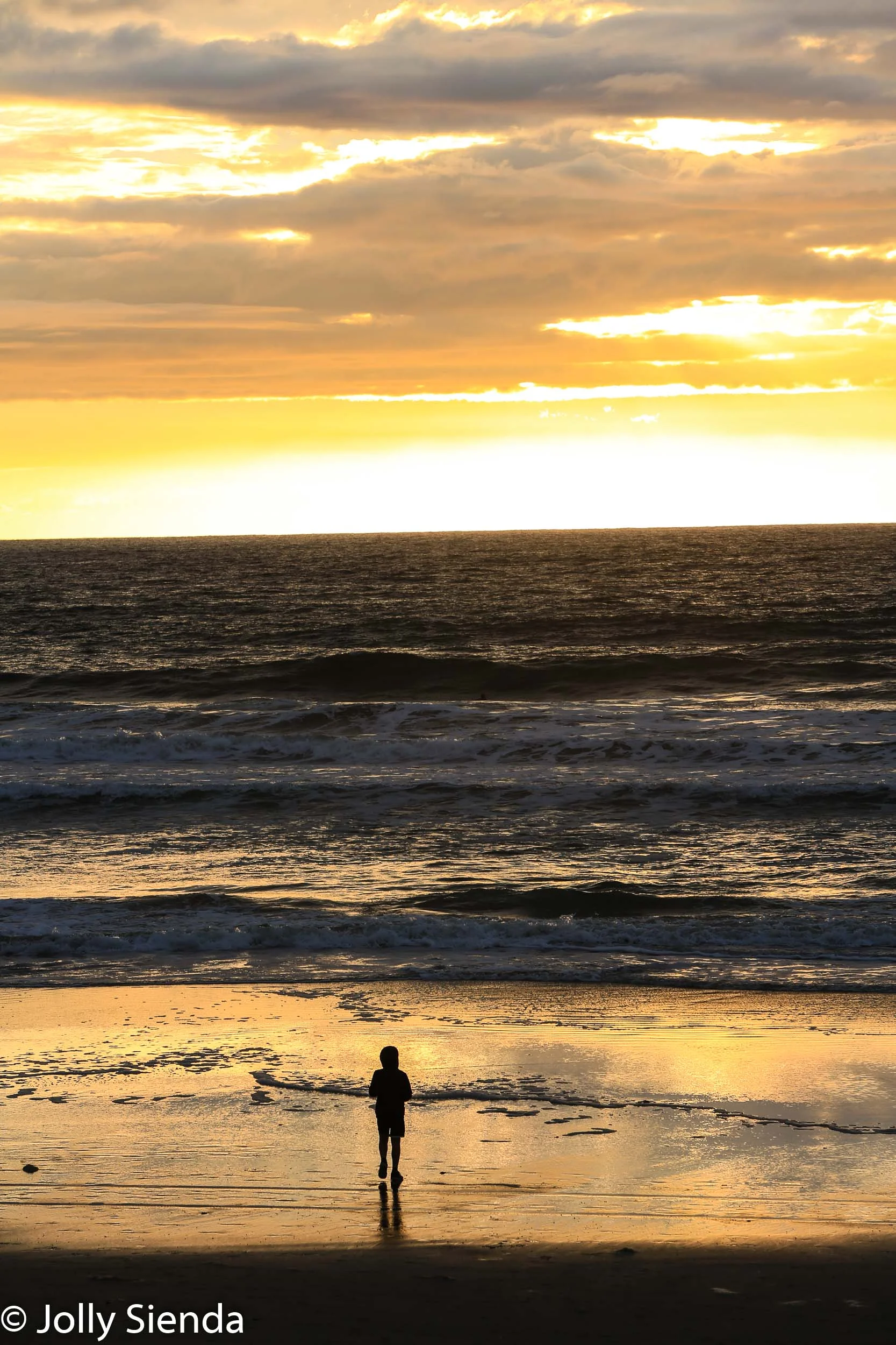 Person in a hoodie watches the sunsets glow on the sand at Torre