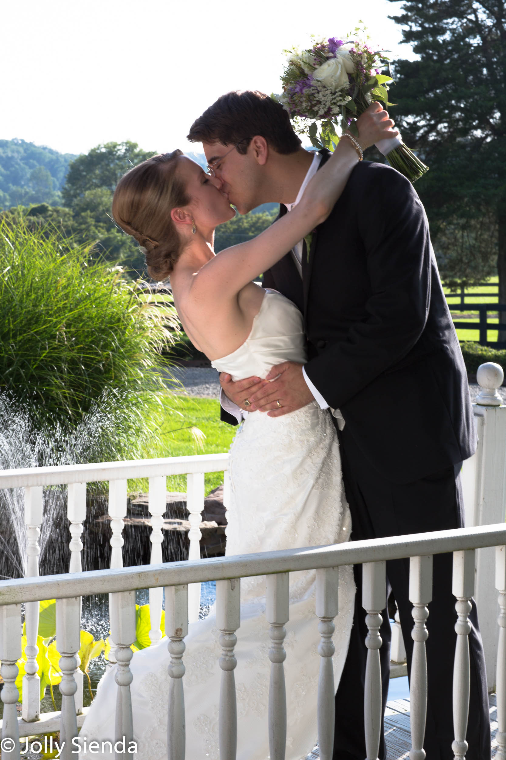 Groom kisses his bride on a bridge overlooking a pond - wedding 