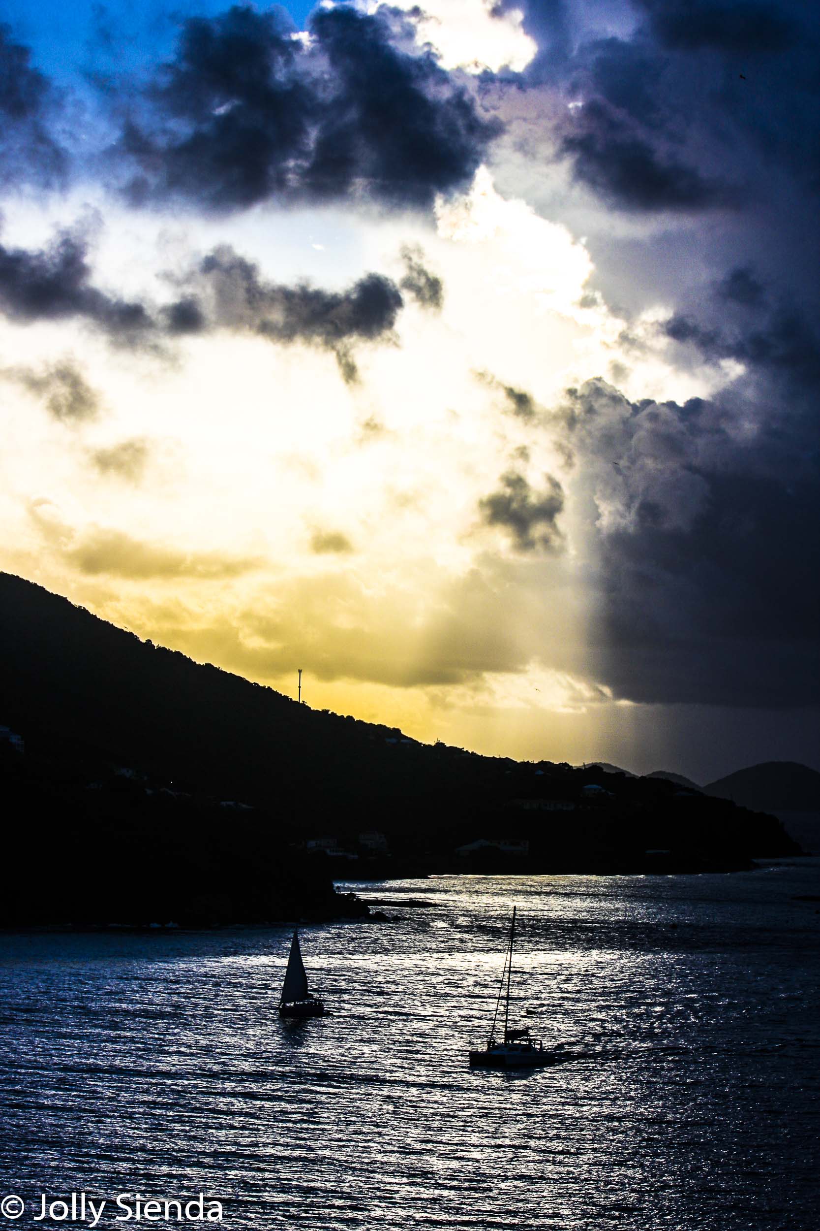 The sun breaks through clouds sending light onto the water, boat