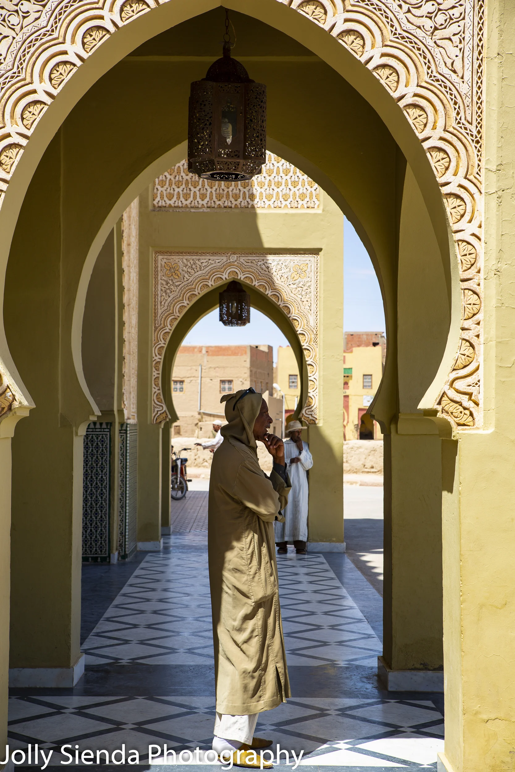 Man in a  djellaba stands in an Islamic archway