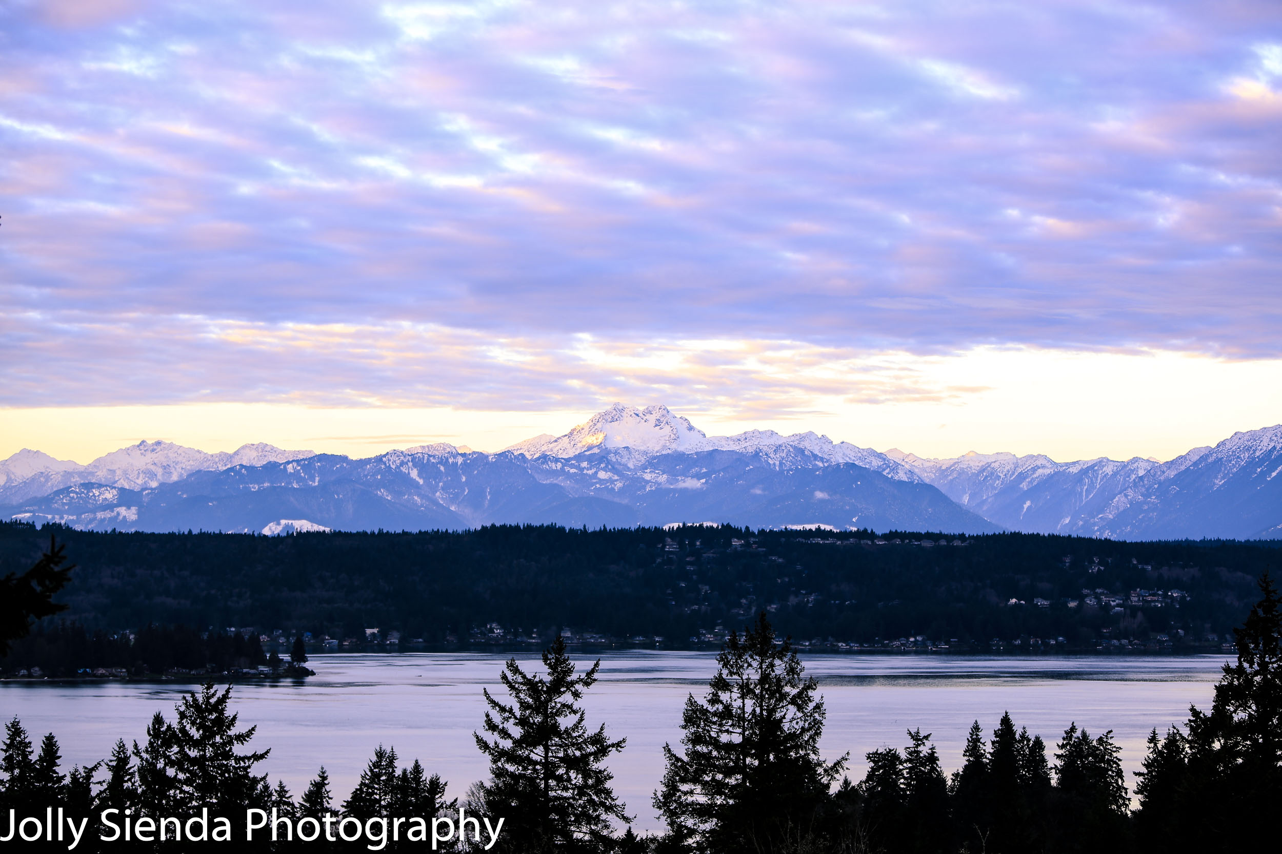 Pastel cumulus clouds rise over snow covered Olympic Mountains a