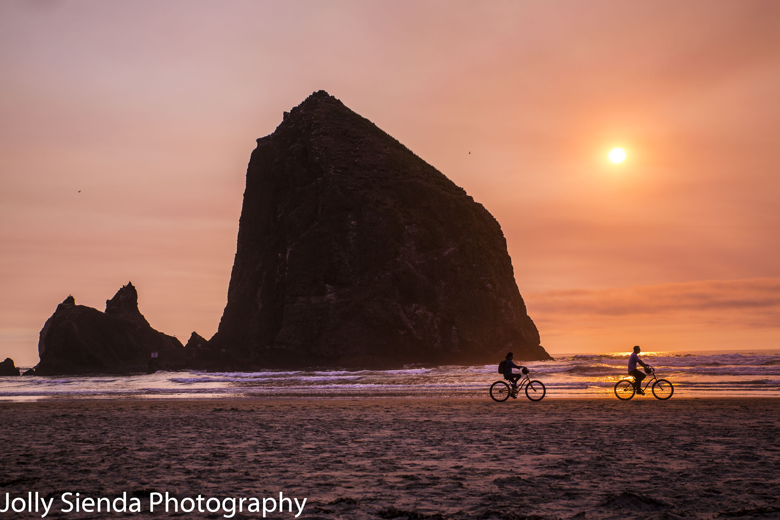 People ride bicycles past Haystack Rocks at sunset