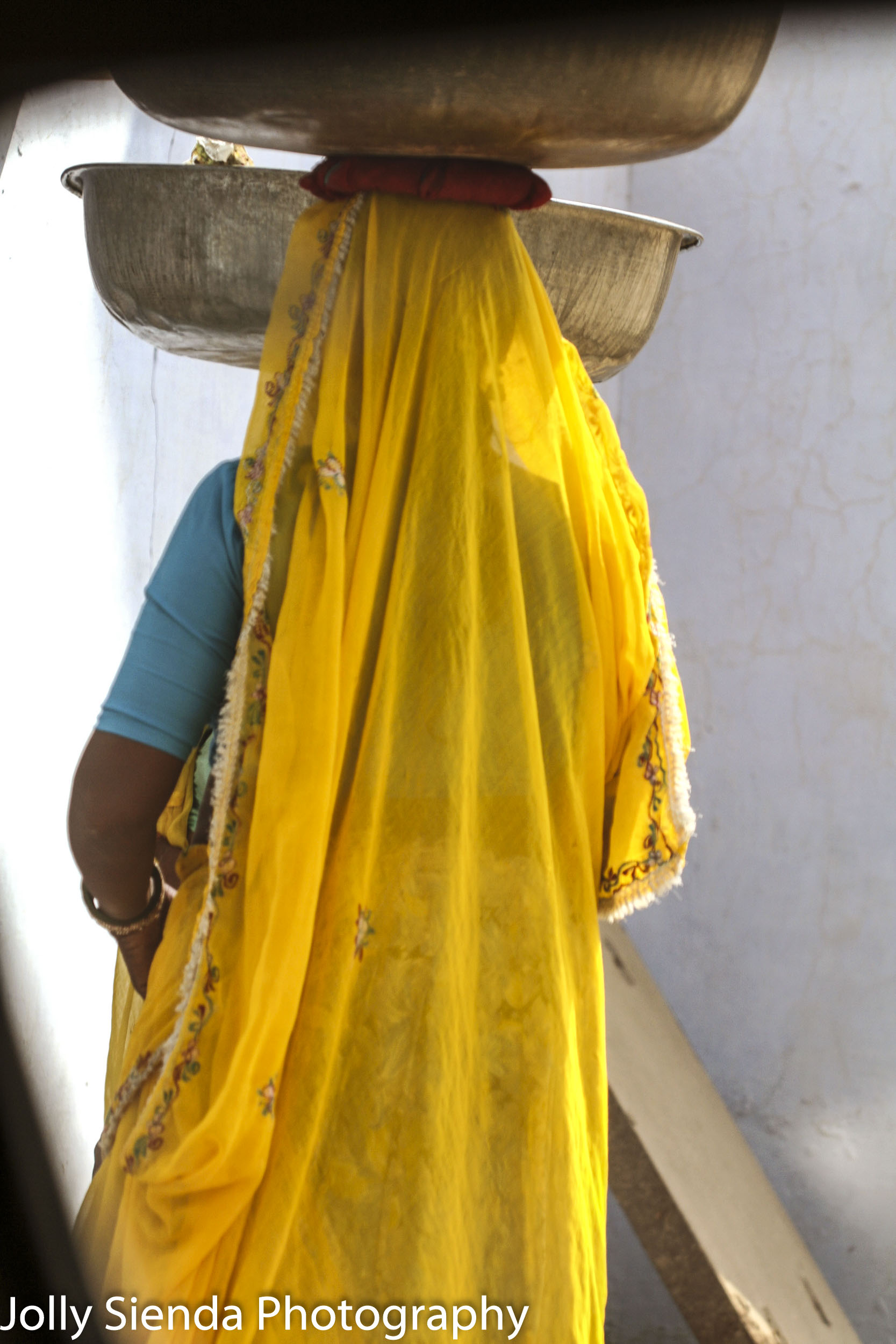 Woman wearing a sari balances copper bowls on her head