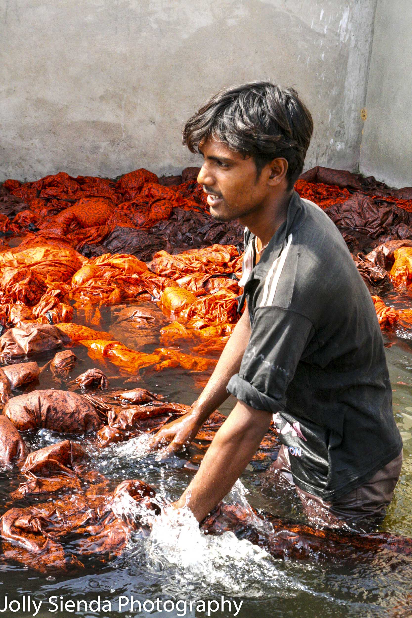 Young man wades in water working dyed block cotton cloth at a fa